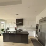 Modern renovated kitchen with white flat-panel cabinetry, a dark center island, stainless steel appliances, and large windows providing natural light